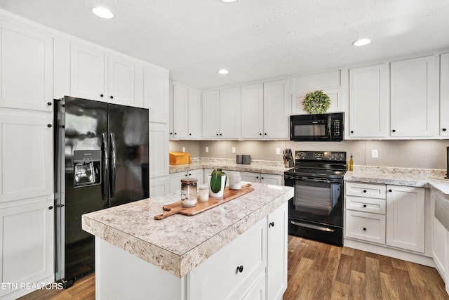 kitchen with white cabinets, black appliances, a center island, and wood-type flooring