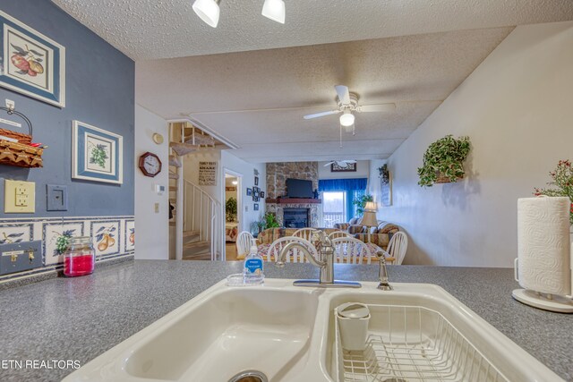 kitchen featuring ceiling fan, sink, a stone fireplace, and a textured ceiling