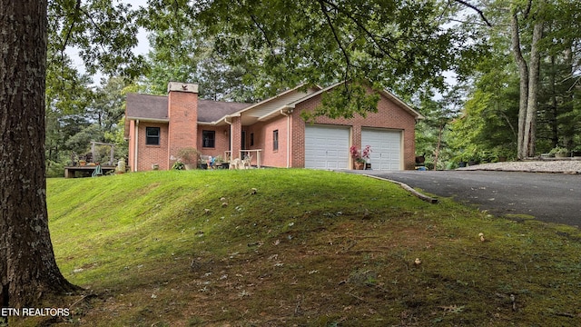 ranch-style home with aphalt driveway, a chimney, a garage, a front yard, and brick siding