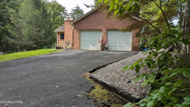 view of property exterior with brick siding, driveway, a garage, and a chimney