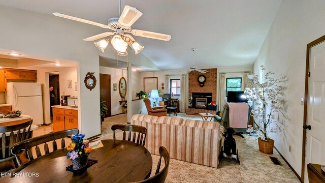 dining space with ceiling fan, brick wall, light colored carpet, and a brick fireplace