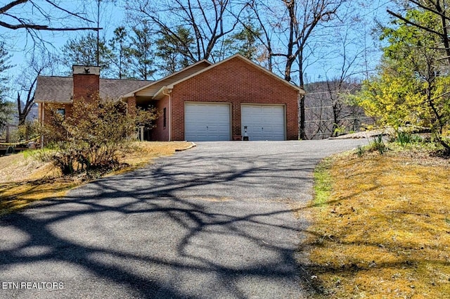view of front of home featuring brick siding, driveway, an attached garage, and a chimney