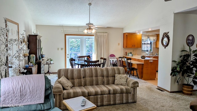 living area with light carpet, vaulted ceiling, ceiling fan, and a textured ceiling