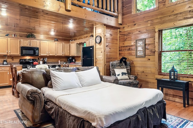 bedroom with black refrigerator, light hardwood / wood-style flooring, and wooden walls