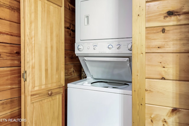 washroom with stacked washing maching and dryer and wooden walls