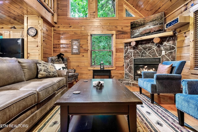 living room featuring wooden walls, wooden ceiling, a stone fireplace, and wood-type flooring