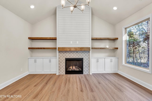 unfurnished living room featuring a tiled fireplace, a notable chandelier, lofted ceiling, and light wood-type flooring