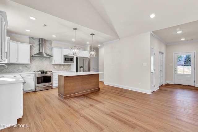 kitchen featuring a kitchen island, white cabinetry, appliances with stainless steel finishes, and wall chimney range hood