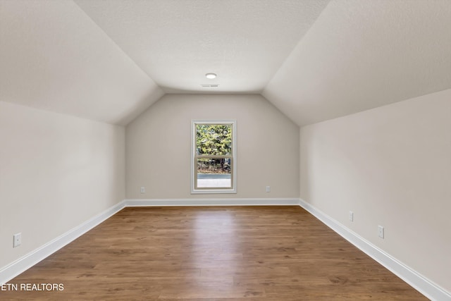 bonus room featuring wood-type flooring, vaulted ceiling, and a textured ceiling