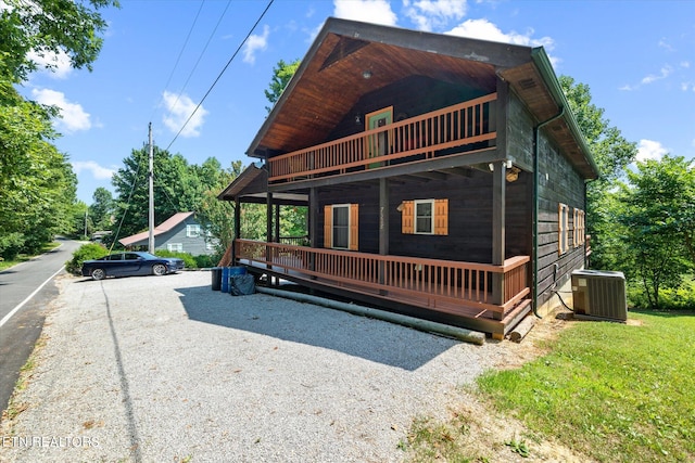 rear view of property with central air condition unit, a balcony, and a lawn