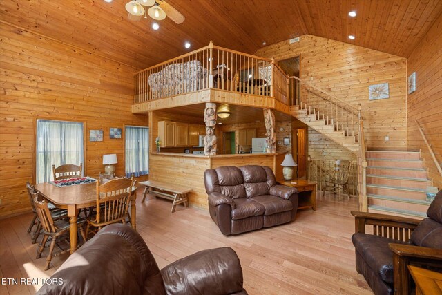 living room with ceiling fan, wood ceiling, wooden walls, high vaulted ceiling, and light hardwood / wood-style floors