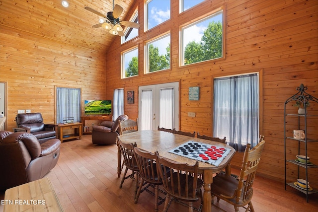 dining room with ceiling fan, high vaulted ceiling, wood walls, french doors, and hardwood / wood-style flooring