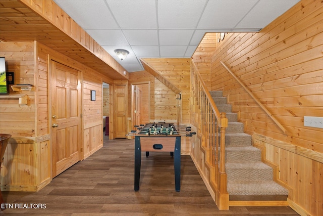 playroom with wood walls, wood-type flooring, and a paneled ceiling