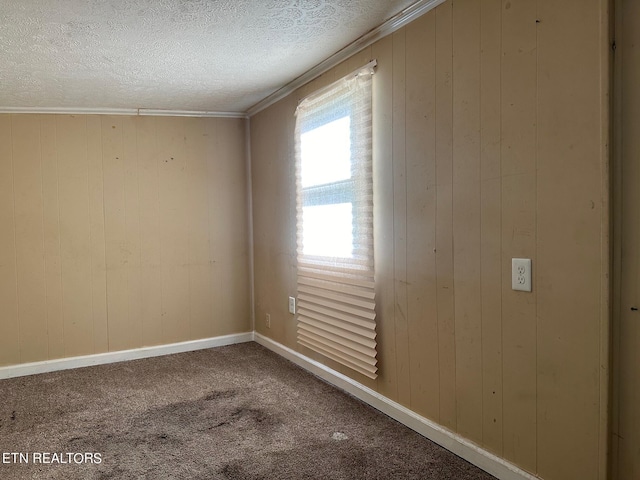 carpeted empty room with a textured ceiling, wooden walls, crown molding, and baseboards