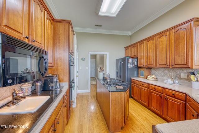 kitchen featuring ornamental molding, sink, tasteful backsplash, black appliances, and light wood-type flooring