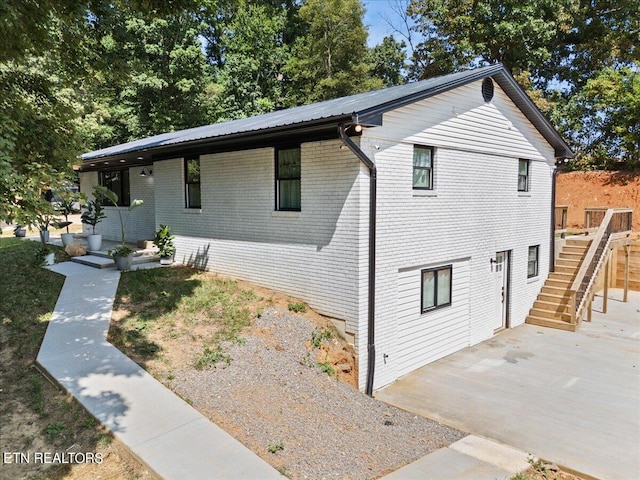 view of front of house featuring metal roof, brick siding, and stairs