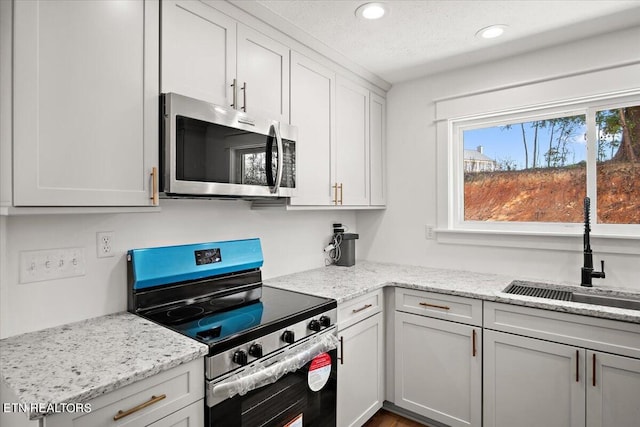 kitchen with a sink, light stone counters, a textured ceiling, recessed lighting, and appliances with stainless steel finishes