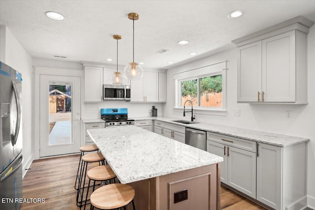 kitchen with light wood finished floors, a kitchen island, a kitchen bar, appliances with stainless steel finishes, and a sink