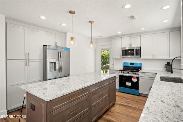 kitchen with light stone counters, visible vents, a sink, appliances with stainless steel finishes, and light wood-type flooring