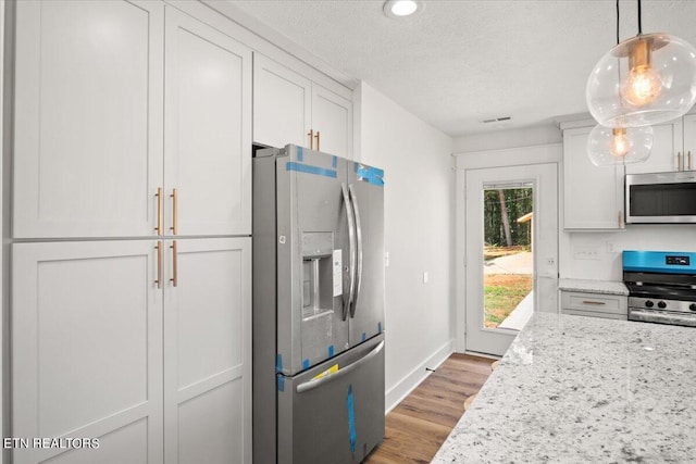 kitchen with light stone countertops, wood finished floors, appliances with stainless steel finishes, a textured ceiling, and white cabinetry