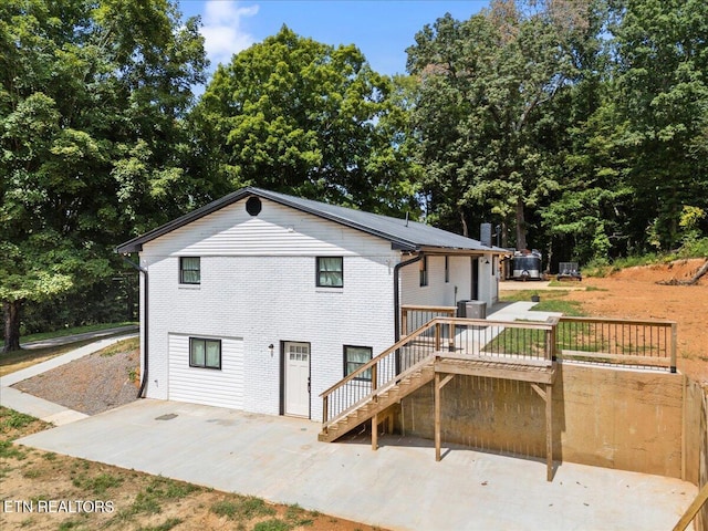 back of property with brick siding, a deck, stairs, and a patio