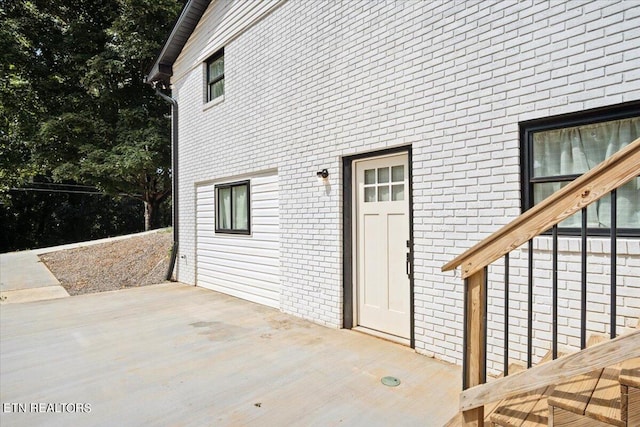 view of exterior entry with brick siding and a patio