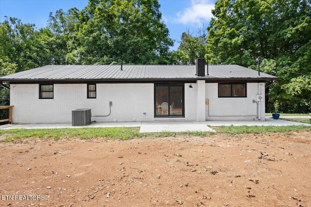 rear view of property featuring a patio, metal roof, brick siding, and a chimney