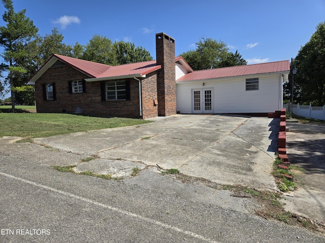 single story home with a chimney, metal roof, french doors, a front lawn, and brick siding