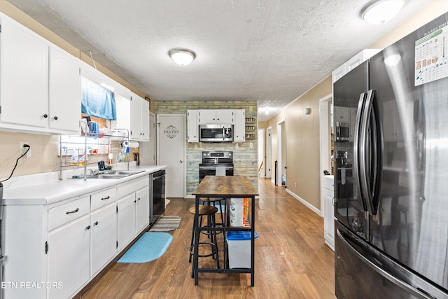 kitchen featuring appliances with stainless steel finishes, light hardwood / wood-style floors, white cabinets, and tasteful backsplash