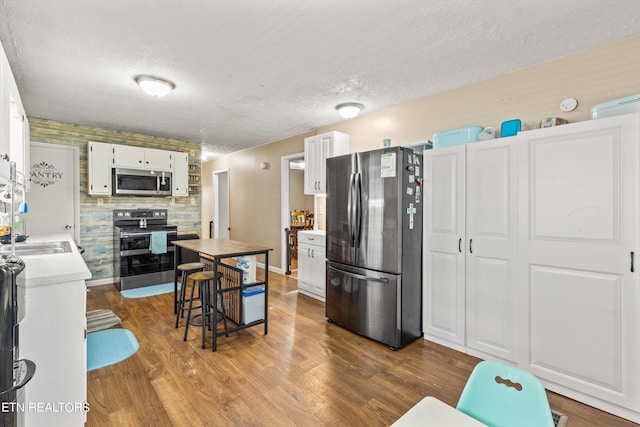 kitchen with hardwood / wood-style floors, sink, appliances with stainless steel finishes, a textured ceiling, and white cabinets