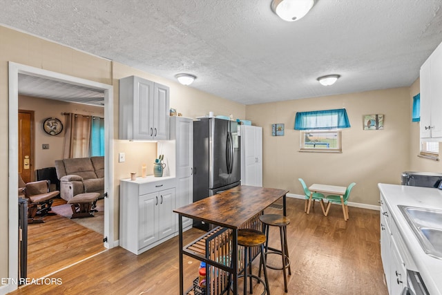 kitchen with a textured ceiling, white cabinetry, hardwood / wood-style flooring, and a breakfast bar area