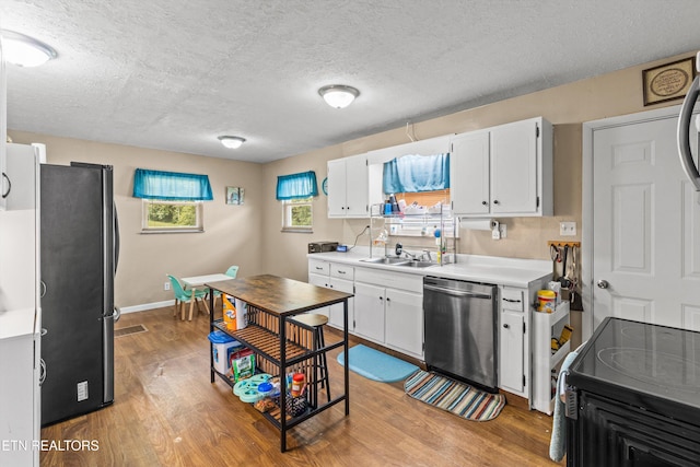 kitchen featuring stainless steel dishwasher, white cabinetry, hardwood / wood-style flooring, a textured ceiling, and black refrigerator