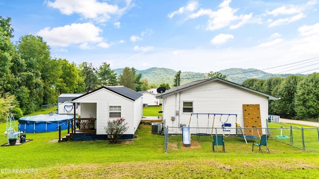 rear view of property featuring cooling unit, a covered pool, an outdoor structure, and a lawn