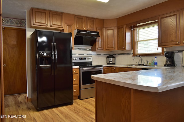 kitchen with a peninsula, light countertops, black fridge, stainless steel range with electric cooktop, and a sink