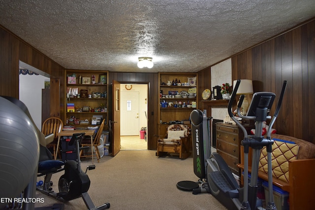 exercise area with a textured ceiling, wood walls, and carpet flooring