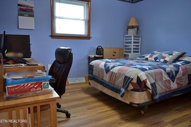 bedroom with baseboards, visible vents, and wood finished floors