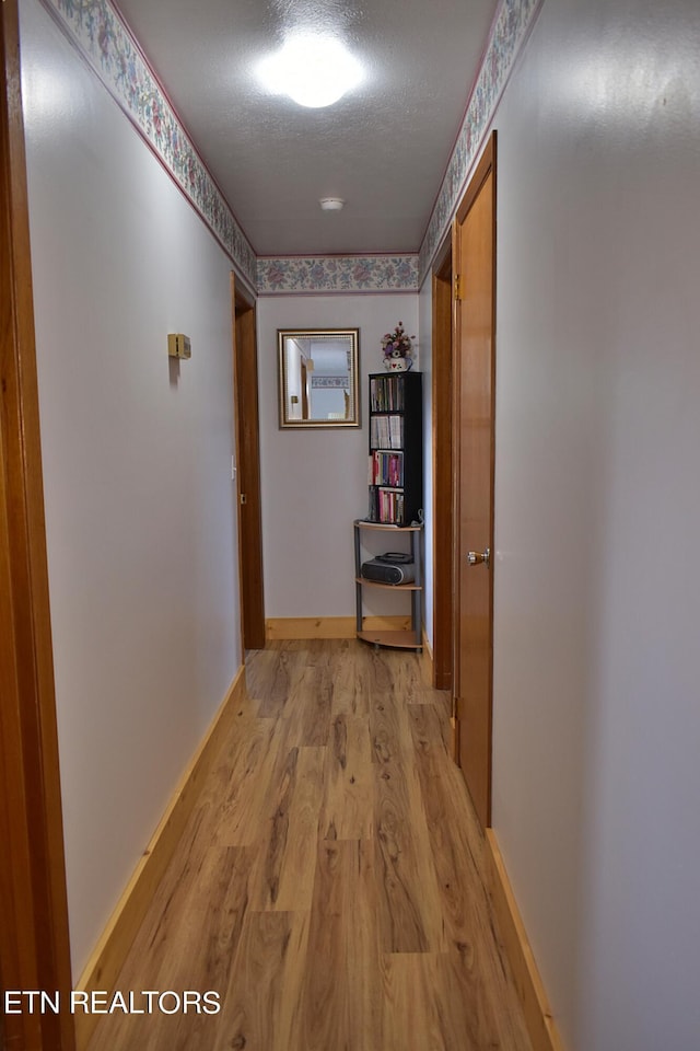 hallway featuring light wood-type flooring, a textured ceiling, and baseboards