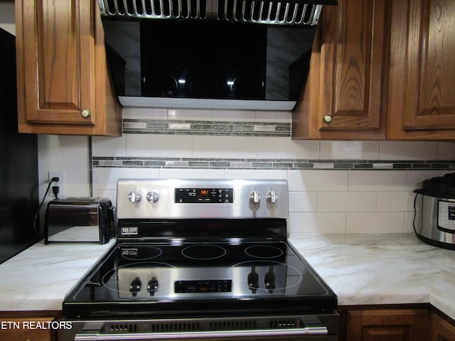 kitchen featuring extractor fan, decorative backsplash, brown cabinets, and electric range oven