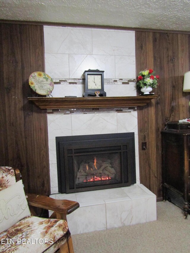 room details featuring a textured ceiling, wood walls, carpet, and a tile fireplace