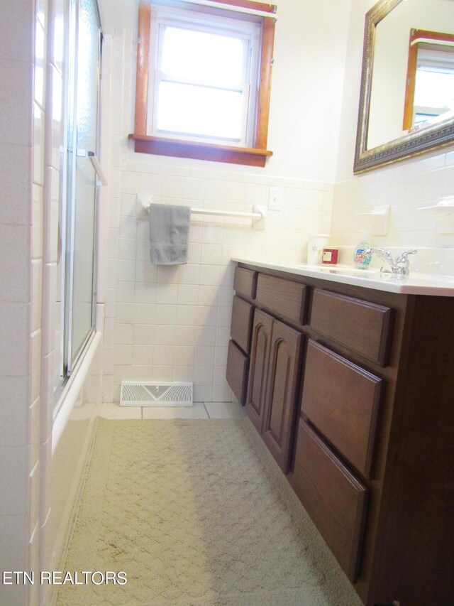 full bath with tile patterned flooring, visible vents, vanity, tile walls, and a shower with door