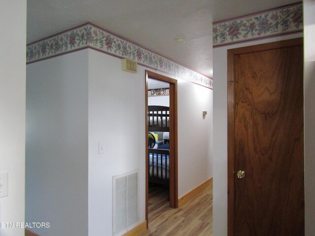 hall with wallpapered walls, light wood-style flooring, and visible vents