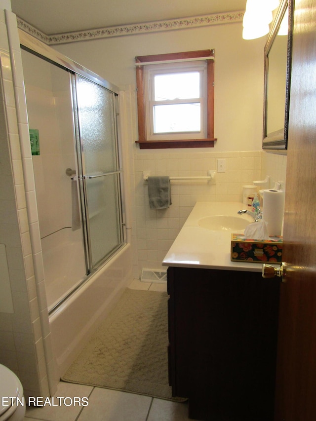 bathroom featuring tile patterned flooring, bath / shower combo with glass door, visible vents, vanity, and tile walls