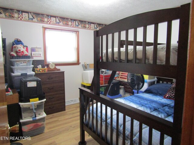 bedroom with visible vents, a textured ceiling, baseboards, and wood finished floors