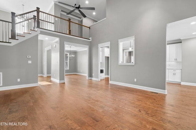 unfurnished living room featuring light hardwood / wood-style flooring, a high ceiling, and ceiling fan with notable chandelier