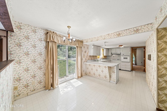 kitchen with white oven, backsplash, a textured ceiling, light tile patterned floors, and kitchen peninsula