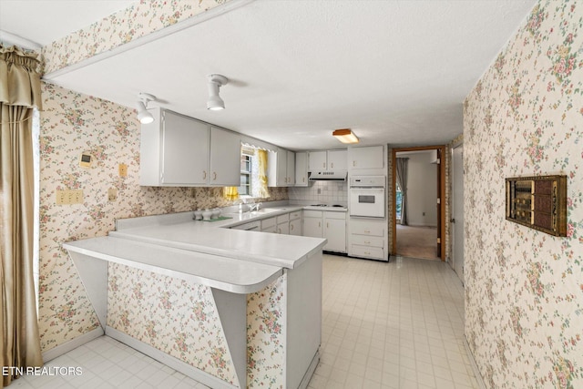 kitchen featuring decorative backsplash, light tile patterned floors, kitchen peninsula, gray cabinets, and oven