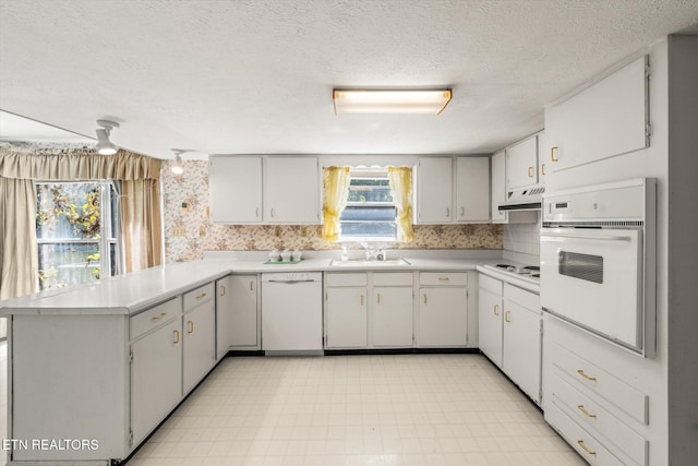 kitchen with sink, white appliances, premium range hood, light tile patterned floors, and kitchen peninsula