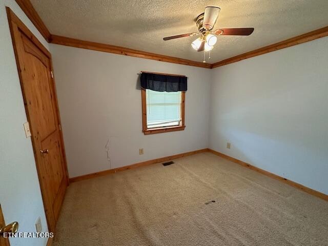 carpeted spare room featuring ceiling fan, ornamental molding, and a textured ceiling