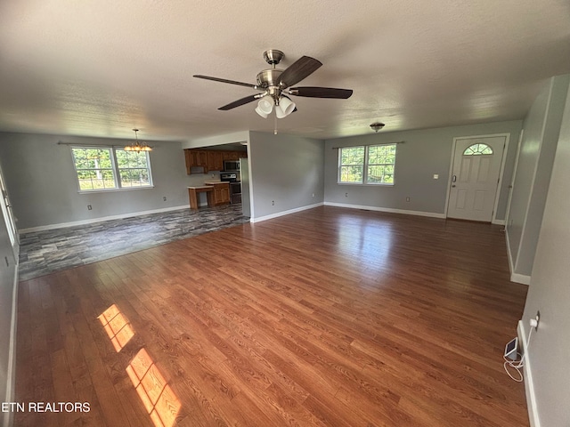 unfurnished living room featuring a textured ceiling, ceiling fan with notable chandelier, plenty of natural light, and dark hardwood / wood-style floors