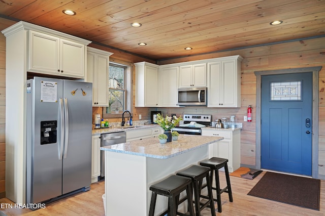 kitchen with a kitchen island, stainless steel appliances, light wood-type flooring, and light stone counters